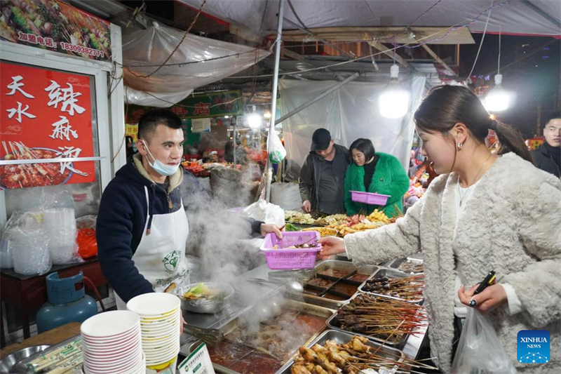 Ιδιοκτήτης ενός πάγκου μαλατάνγκ, εξυπηρετεί έναν πελάτη σε έναν δρόμο με σνακ στην πόλη Τιενσουέι της επαρχίας Γκανσού, στις 19 Μαρτίου του 2024. (Φωτογραφία / Xinhua)