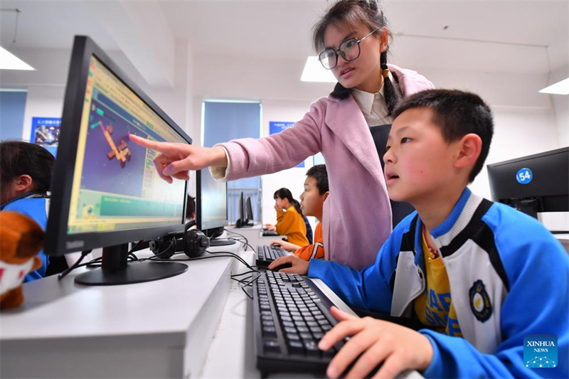 Δασκάλα δίνει οδηγίες καθώς ένας μαθητής χρησιμοποιεί τον υπολογιστή στο μάθημα προγραμματισμού στην πόλη Σιανγκτάν της επαρχίας Χουνάν. (Φωτογραφία / Xinhua)